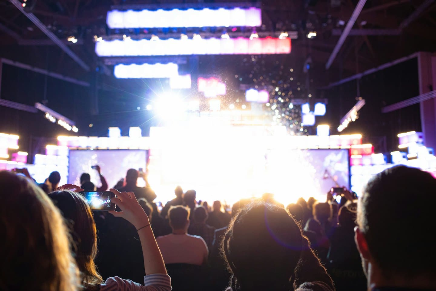 Audience silhouetted against bright stage lights recording a performance.