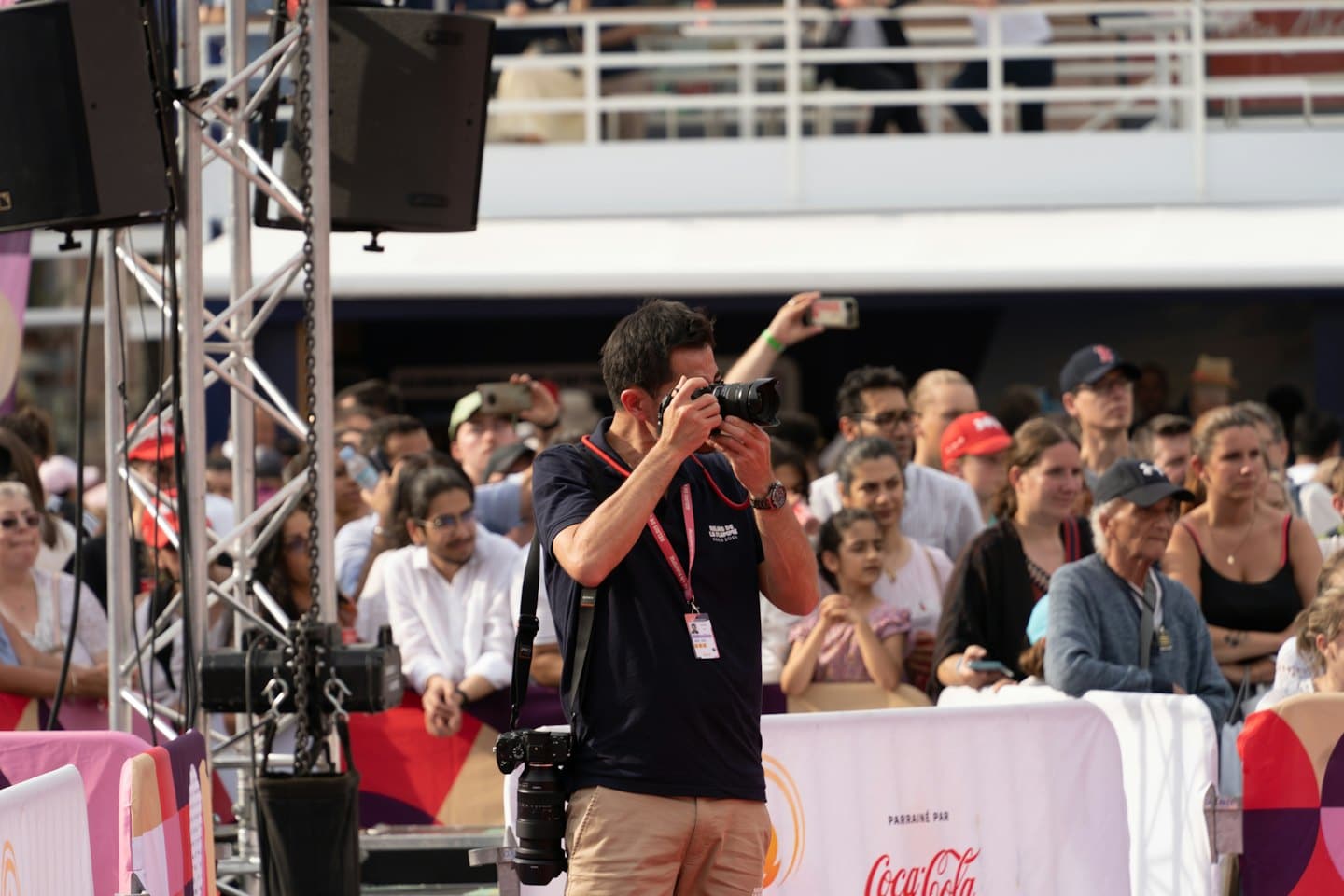 Man with DSLR camera at an outdoor event behind a barrier.