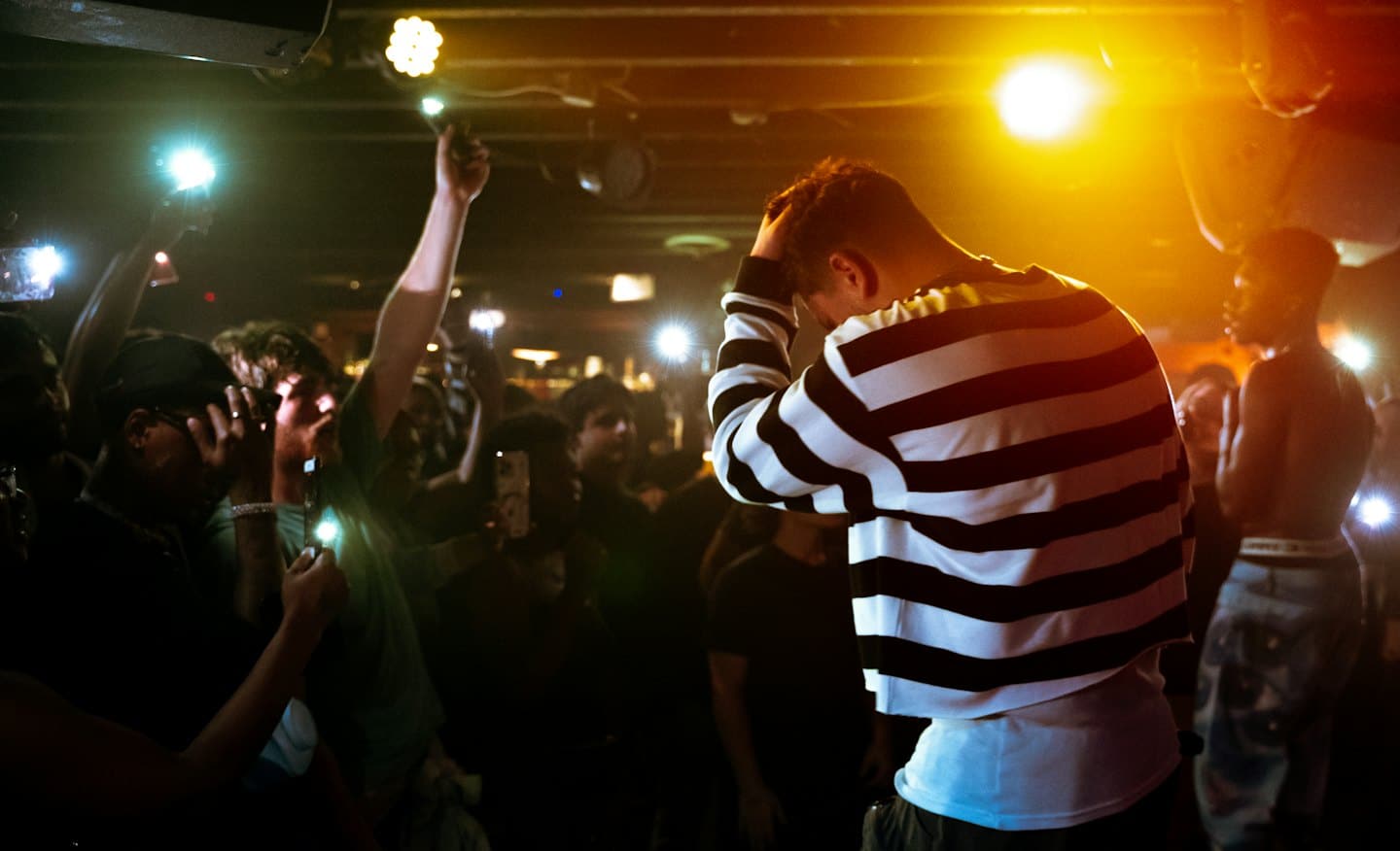 Concert audience cheers while holding illuminated mobile phones.